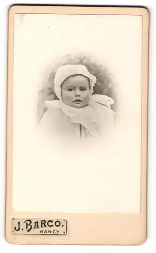 Fotografie J. Barco, Nancy, kleines Baby im weissen Kleid und Mütze