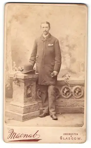 Fotografie Macnab, Uddingston, Herr im Mantel und Hut auf einer Brüstung