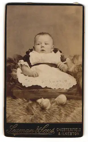 Fotografie Seaman & Sons, Chesterfield, Portrait zuckersüsses Baby im bestickten Kleidchen
