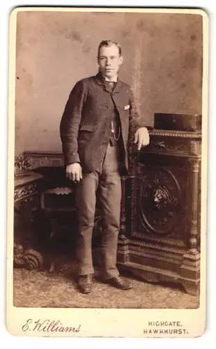 Fotografie E. Williams, Hawkhurst, Mann an Kommode lehnend