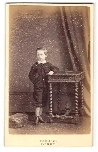 Fotografie Clement Rogers, Derby, Portrait hübsch gekleideter Junge an Tisch gelehnt