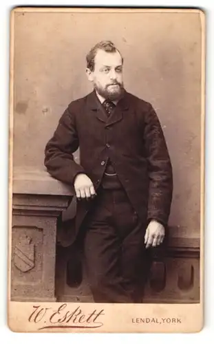 Fotografie W. Eskett, York, Portrait elegant gekleideter Herr mit Bart an Sockel gelehnt