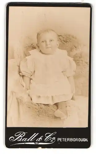 Fotografie Ball & Co., Peterborough, Portrait niedliches Baby im weissen Kleidchen