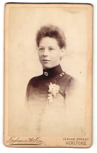 Fotografie Ladmore & Son, Hereford, Portrait lächelnde hübsche Dame mit Ansteckblume