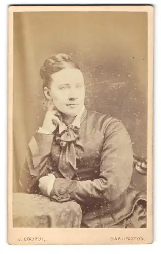 Fotografie J. Cooper, Darlington, Portrait bürgerliche Dame mit Flechtfrisur am Tisch sitzend