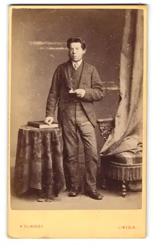 Fotografie R. Slingsby, Lincoln, Portrait modisch gekleideter Herr mit Zettel an Tisch gelehnt
