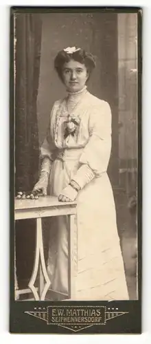 Fotografie E. W. Matthias, Seifhennersdorf, Portrait bürgerliche Dame mit Blumen an Tisch gelehnt