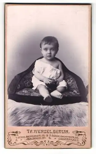 Fotografie Th. Wenzel, Berlin, Kleinkind in weissem Kleidchen sitzt auf Sitzkissen welches auf Fell liegt
