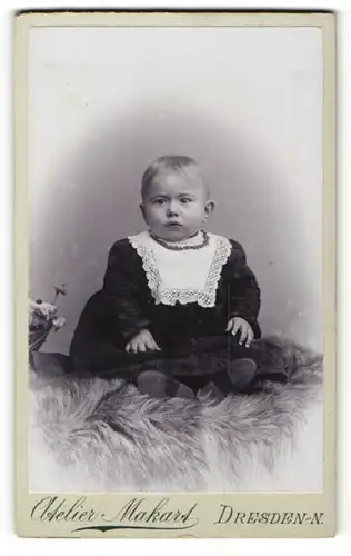Fotografie Atelier Makart, Dresden-N, Portrait niedliches Kleinkind im hübschen Kleid auf Fell sitzend
