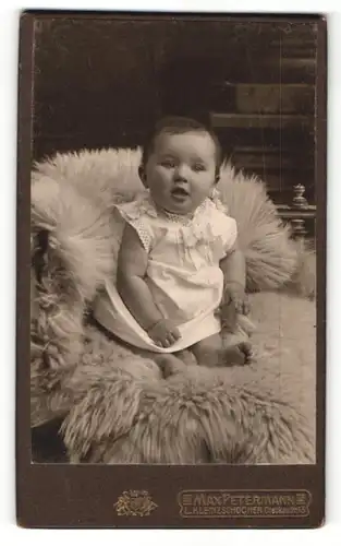 Fotografie Max Petermann, Leipzig-Kl. Zschocher, Portrait niedliches Kleinkind im weissen Hemd auf Fell sitzend