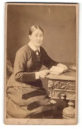 Fotografie A. T. Osbourne, Lincoln, Portrait bürgerliche Dame mit Medaillon und Buch am Tisch sitzend