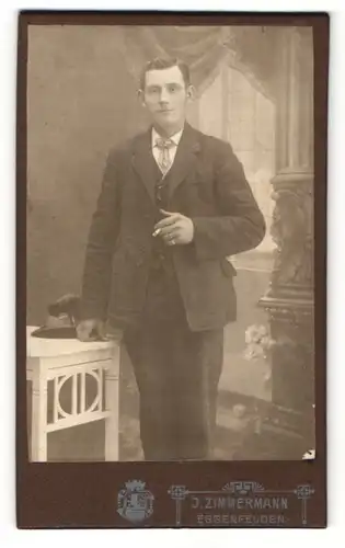 Fotografie J. Zimmermann, Eggenfelden, Portrait junger Herr im Anzug mit Zigarette an Tisch gelehnt