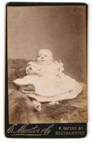 Fotografie E. Mentor, Southampton, Portrait süsses Baby im weissen Taufkleidchen