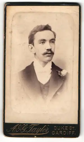 Fotografie A. & G. Taylor, Cardiff, Portrait junger Herr im Anzug mit Ansteckblume und Schnurrbart