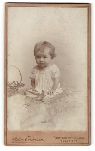 Fotografie Atelier Erdmann, Darmstadt, Kleinkind in weissem Kleidchen sitzt neben einem Korb auf einem Fell