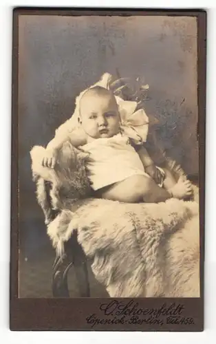 Fotografie O. Schoenfeldt, Berlin, Baby in weissem Laibchen sitzt auf Fell welches auf Stuhl liegt