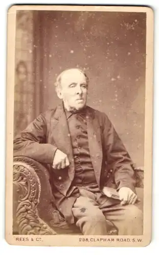 Fotografie Rees & Co., London, älterer Mann mit Buch in der Hand im Anzug auf Sessel sitzend