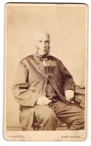 Fotografie J. Cooper, Darlington, Mann mit Koteletten im Anzug auf Stuhl sitzend