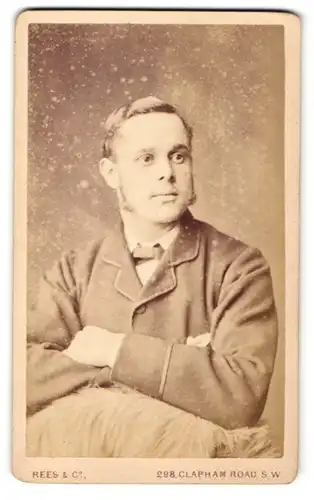 Fotografie Rees & Co., London-SW, Portrait bürgerlicher Herr mit Fliege und Backenbart an Fell gelehnt