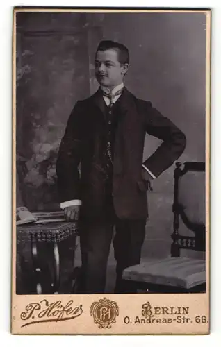 Fotografie P. Höfer, Berlin-O, Portrait junger Herr im Anzug mit Krawatte an Tisch gelehnt
