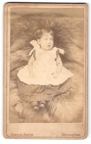 Fotografie Joseph Norris, Birmingham, Portrait niedliches Kleinkind im hübschen Kleid auf Fell sitzend