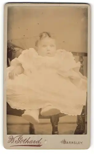 Fotografie Warner Gothard, Barnsley, kleines baby in weissem Kleid auf Stuhl sitzend