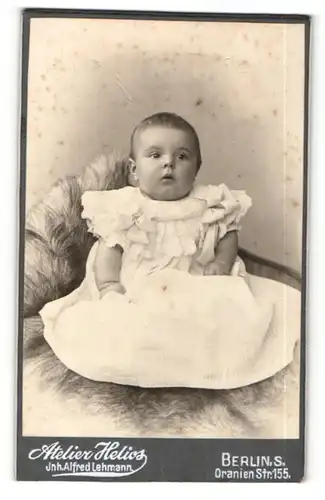 Fotografie Alfred Lehmann, Berlin-S, Portrait niedliches Kleinkind im weissen Kleid auf Fell sitzend