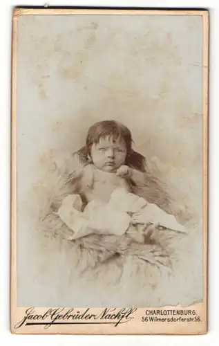 Fotografie Jacob Gebrüder Nachfl., Berlin-Charlottenburg, Portrait niedliches Baby mit kurzen Haaren auf Fell sitzend