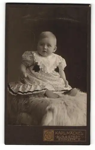 Fotografie Karl Mäckel, Burgstädt, Baby in Kleid auf Tierfell sitzend