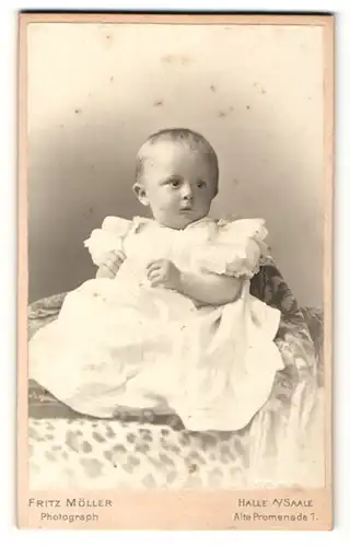 Fotografie Fritz Müller, Halle a / Saale, Portrait sitzendes Kleinkind im weissen Kleid mit kurzen Haaren