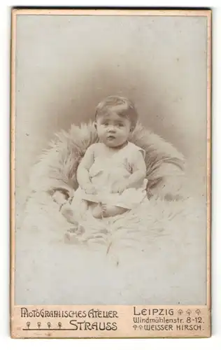 Fotografie Atelier Strauss, Leipzig, Portrait niedliches Kleinkind im weissen Hemd auf Fell sitzend