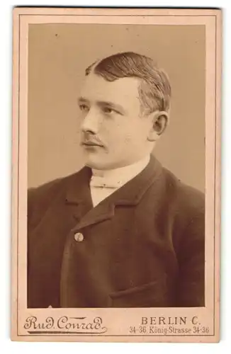 Fotografie Rud. Conrad, Berlin, Portrait eines Mannes mit Mittelscheitel in dunkler Anzugjacke