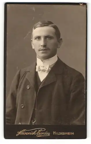 Fotografie Heinrich Cordes, Hildesheim, Portrait eines feinen jungen Herren in Anzug mit schicker Schleife