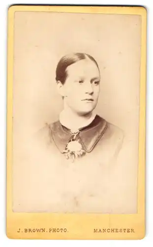 Fotografie J. Brown, Manchester, Portrait dunkelhaariges Fräulein mit Brosche und Blume am Kragen