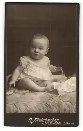 Fotografie R. Steinbacher, Salzwedel, Portrait niedliches Baby im Hemdchen auf Fell sitzend