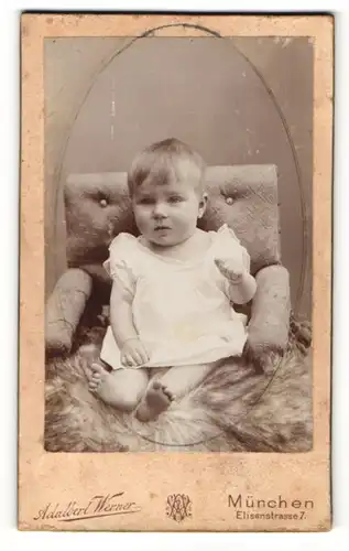 Fotografie Adalbert Werner, München, Kleinkind im gerüschten Hemdchen sitzt auf Felldecke