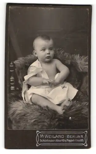 Fotografie M. Weiland, Berlin-N, Portrait niedliches Kleinkind im weissen Hemd auf Fell sitzend