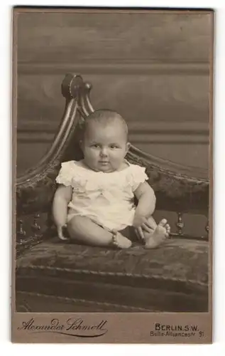 Fotografie Alexander Schmoll, Berlin-SW, Portrait sitzendes Baby im weissen Hemd mit nackigen Füssen
