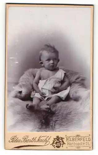 Fotografie Peter Barth Nachf., Elberfeld, Portrait niedliches Kleinkind im weissen Hemd auf Fell sitzend