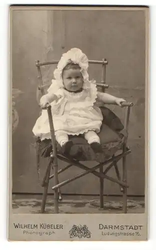 Fotografie Wilhelm Kübeler, Darmstadt, Portrait sitzendes Kleinkind im weissen Kleid mit Haube