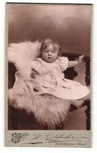 Fotografie H. Goldbecker, Gütersloh i. Westf., Portrait niedliches Kleinkind im weissen Hemd auf Fell sitzend