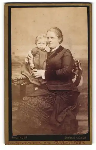 Fotografie Hugo Huth, Schmalkalden, Portrait einer hübschen Mutter in schwarzem Kleid mit süssem Kleinkind im Arm