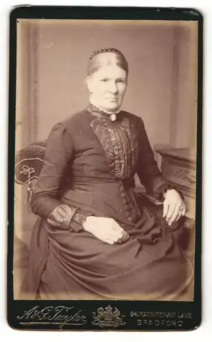 Fotografie A. & G. Taylor, Bradford, Dame mit auf dem Kopf geflochtenen Haaren trägt dunkles Kleid mit weissem Zierkragen