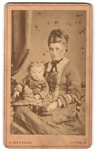 Fotografie C. Metzner, Cottbus, Portrait hübsch gekleidete Dame mit Kleinkind auf dem Schoss