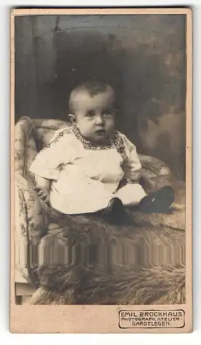 Fotografie Emil Brockhaus, Gardelegen, Portrait niedliches Kleinkind im hübschen Kleid auf Fell sitzend