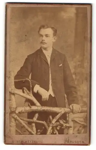 Fotografie Gustav Wetzel, Dresden, Portrait charmanter Herr mit Schnäuzer am Holzzaun stehend