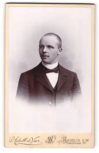Fotografie Achill de Veer, Berlin-SW, Portrait junger Herr mit geschorenem Haar in Anzug mit Fliege