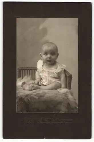 Fotografie G. Vierecke, Hamburg, Portrait niedliches Kleinkind im Hemdchen auf Fell sitzend