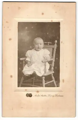 Fotografie Adolph Richter, Leipzig-Lindenau, Portrait eines Kleinkindes im weissen Kleid auf einem Stuhl sitzend