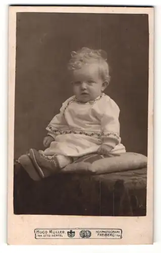 Fotografie Hugo Müller, Freiberg i / Sa., Portrait niedliches Kleinkind im hübschen Kleid auf Kissen sitzend